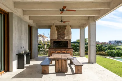 Comedor exterior con mesa de madera rústica, bancos y parrilla — proyecto Gray Rock, por BAS Y GARCIA , en Escobar